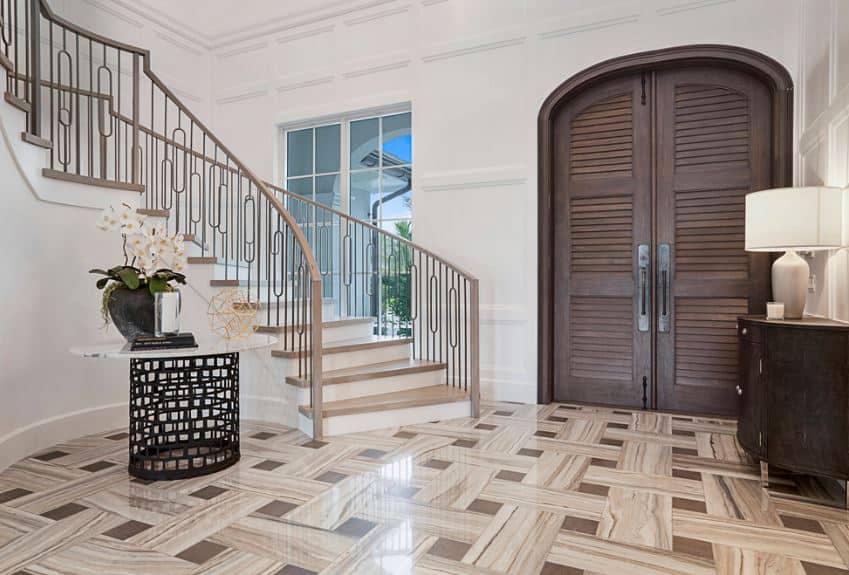 棕色图案的大理石地板与木质大门以及侧面的抽屉完美匹配，抽屉上有一盏台灯，对面是浅棕色和白色的楼梯。