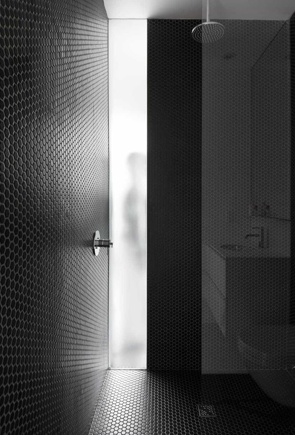 这个淋浴区拥有小的黑色六角形瓷砖，主导着墙壁和地板。淋浴区与浴室的其余部分由半面玻璃墙隔开。