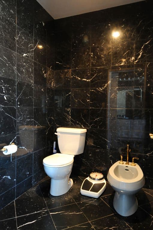 这个黑色大理石瓷砖的浴室有一个纯白色的陶瓷马桶，在光滑的黑色背景下脱颖而出。