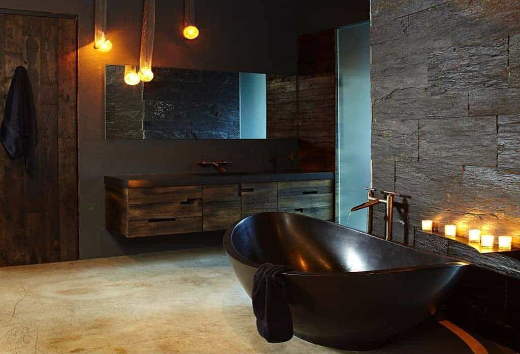 有一个迷人的光滑的黑色独立浴缸，在米黄色大理石地板和有纹理的黑色石墙的映衬下格外引人注目。