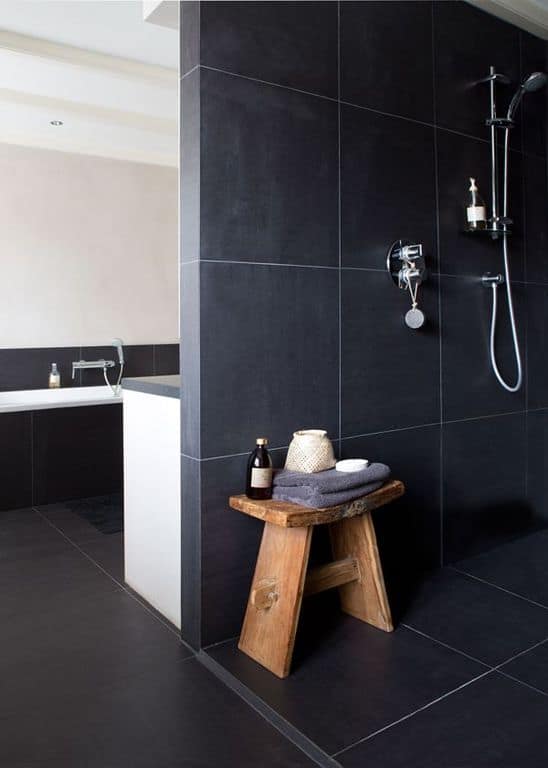 墙壁和地板的黑色瓷砖与银色金属淋浴装置和可爱的木凳搭配在一起。