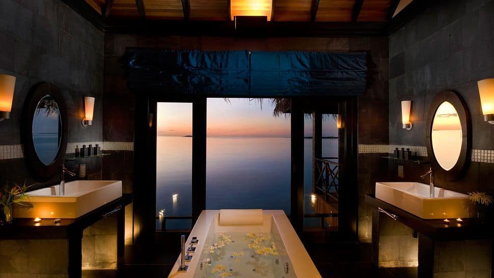 这个迷人的浴室通过大玻璃门强调了热带环境。浴缸两侧是两个带有白色水槽的梳妆台。