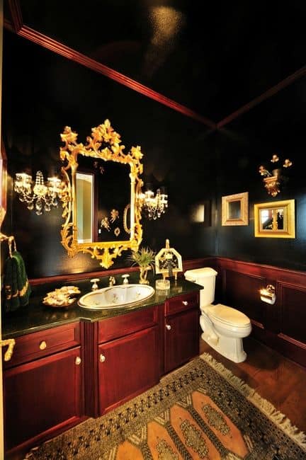这个浴室的黑色墙壁被复杂的梳妆镜和壁挂灯的金色色调所照亮。