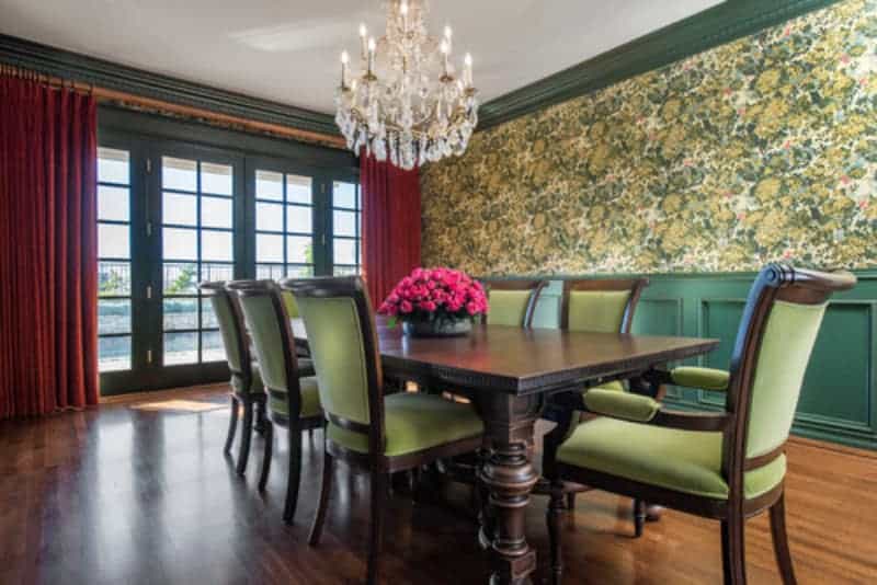 自然光从法式玻璃门射进来，照亮了硬木地板和绿色花卉墙，与餐椅的绿色靠垫相呼应。