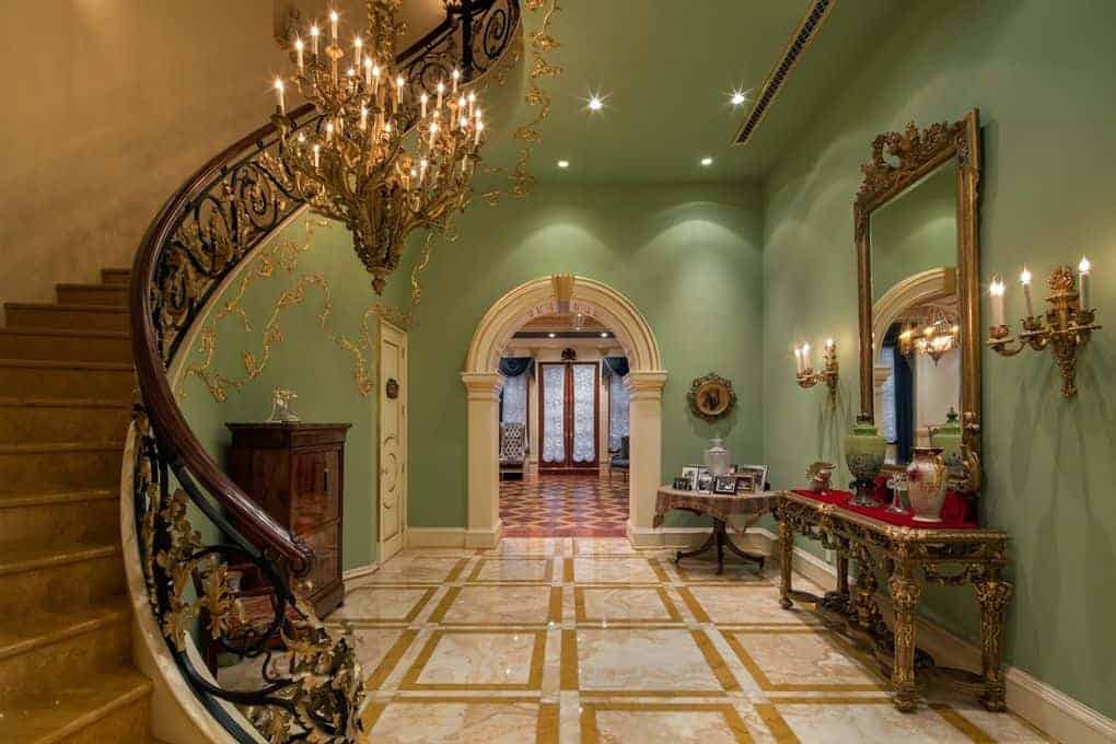 一个优雅的门厅以绿色、金色和白色为特色。它提供了一个令人惊叹的吊灯和华丽的楼梯扶手。