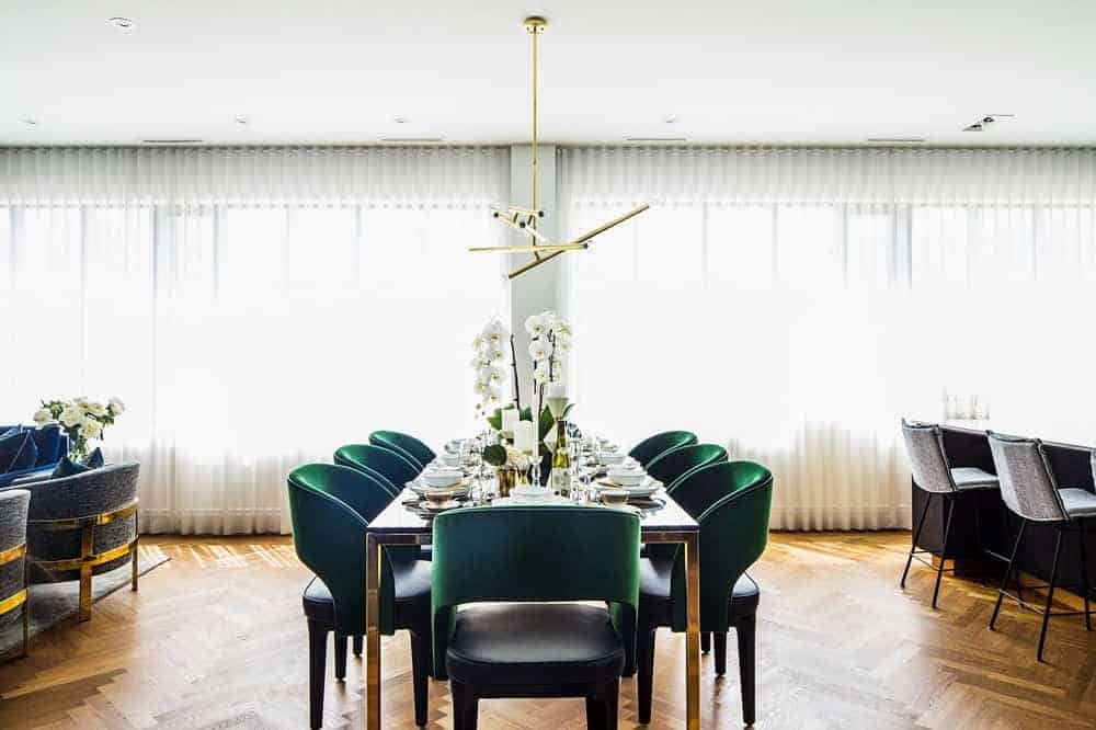 过渡风格的开放式餐厅，矩形餐桌上方有吊灯照明，绿色餐椅可供八人用餐。