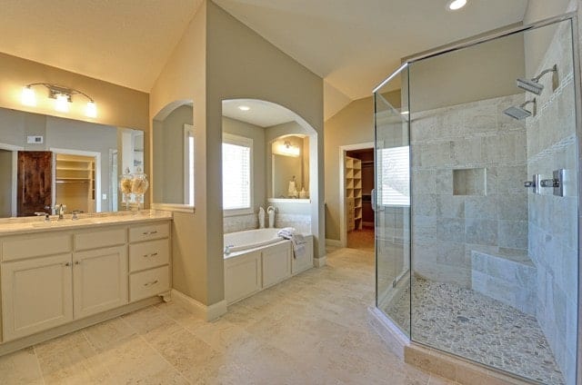 这是一个宽敞而豪华的浴室，有一个大的玻璃封闭淋浴区。在这扇门的对面是浴缸，它被放置在米色梳妆台旁边靠窗的一个迷人的凹室里。