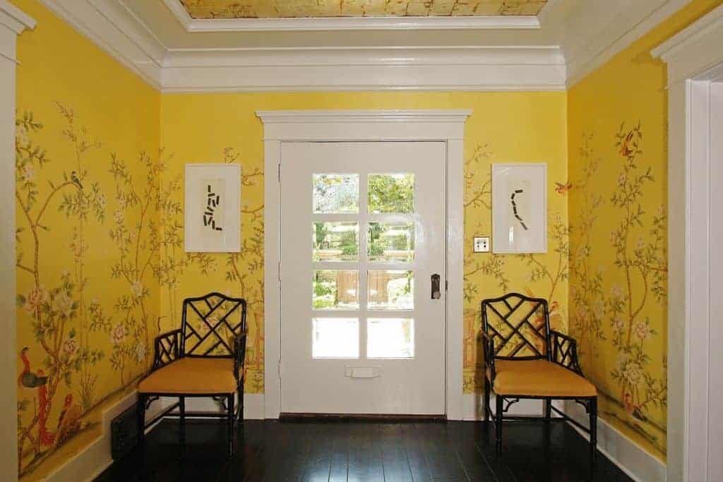 一个小门厅，有装饰的黄色墙壁和托盘天花板。两边有两个座位，放在硬木地板上。