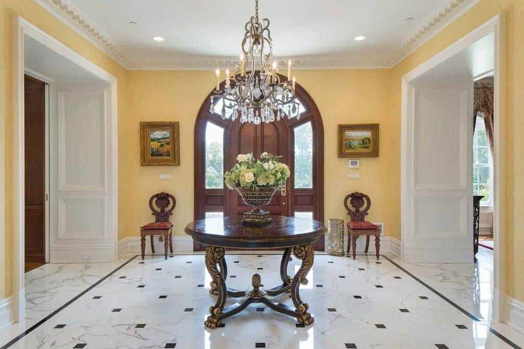 这个门厅拥有优雅的大理石瓷砖地板，中间有一个花哨的餐桌，设置在华丽的吊灯下面。