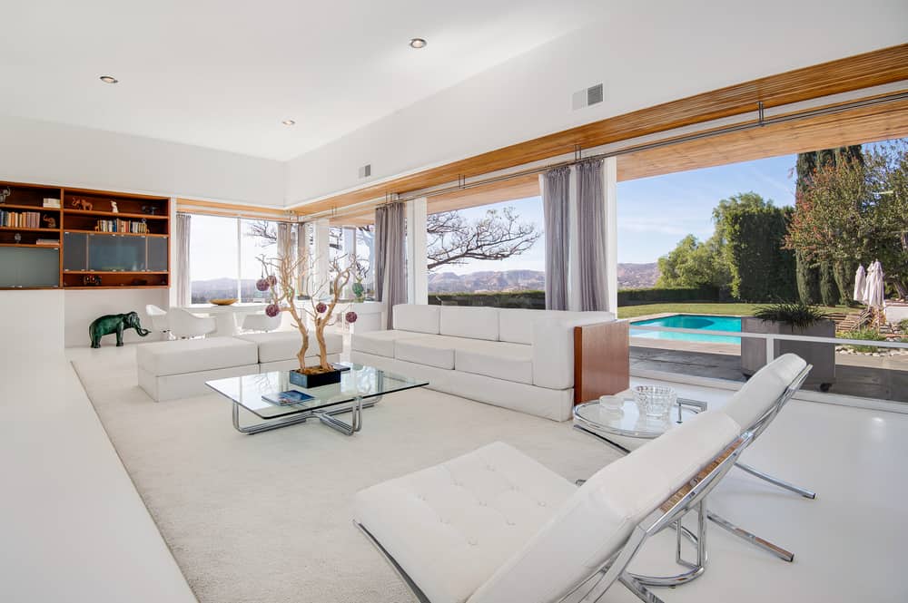 这栋位于洛杉矶的住宅曾经是弗兰克·辛纳屈(Frank Sinatra)的所有，拥有明亮的客厅，白色组合沙发，带金属腿的玻璃台面咖啡桌，以及玻璃墙，可以不间断地看到后院游泳池区域和圣费尔南多谷。白色的décor延伸到白色地板上的小地毯。这座世纪中叶的现代经典建筑由建筑师威廉·佩雷拉设计，曾被拍成多部电视剧和电影，包括《广告狂人》、《加州靡情》、《大小谎言》和《中了魔》。