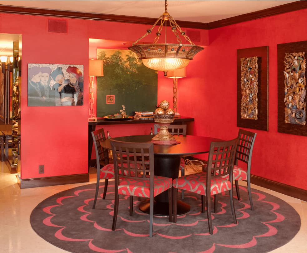 红色的餐厅装饰着华丽的墙壁艺术和黄铜枝形吊灯，悬挂在圆形地毯上的木制餐具上。