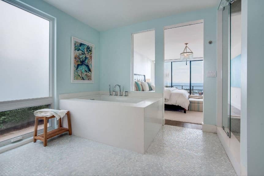 浴缸上方浅绿色墙壁上的彩色花卉画为浴缸外壳、地板以及白色天花板的白色和浅灰色色调增添了一抹色彩。