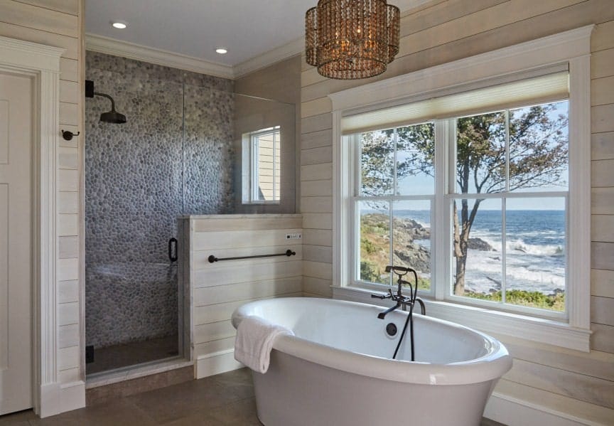 这个主浴室的独立浴缸被别致的天花板灯照亮，通过窗户可以看到令人放松的海景。