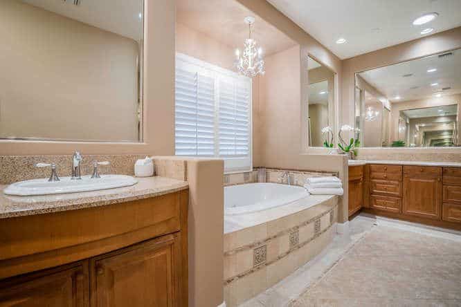 近距离观察主浴室，木质洗手台和无框镜子之间有一个落地式浴缸。