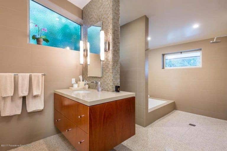 现代浴室拥有宽敞的淋浴区和木制洗手台，配有一面无框镜子，两侧是线性壁灯。
