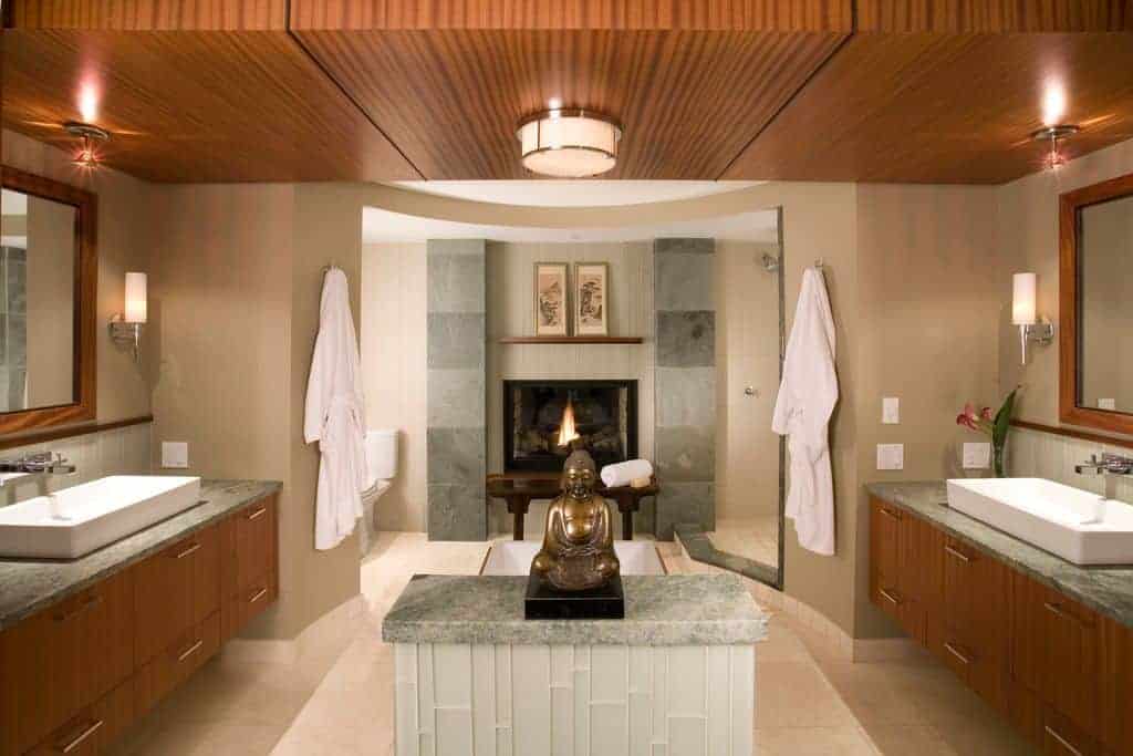 迷你佛像为这间米色浴室带来了经典的焦点，浴室设有壁炉和浮动洗手台，与装有抽水灯的木镶板天花板相辅相成。
