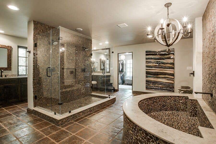 豪华主浴室设有一个玻璃封闭的淋浴区，周围是深色的木质梳妆台和一个深浸泡浴缸，由球形吊灯照明。