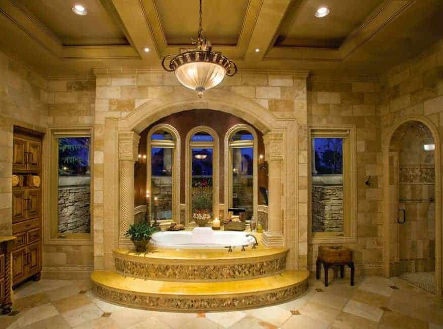 精致的主浴室，石灰石地板和镶有凹形和吊灯的格子天花板。它包括一个用拱形窗户和砖柱包裹的浴缸。