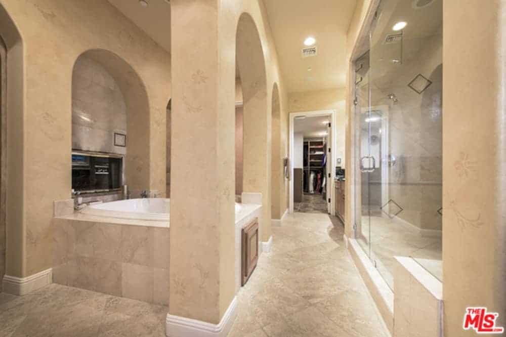 米色主浴室设有步入式衣橱和玻璃封闭的淋浴区。它包括一个大理石瓷砖的开放式浴缸。