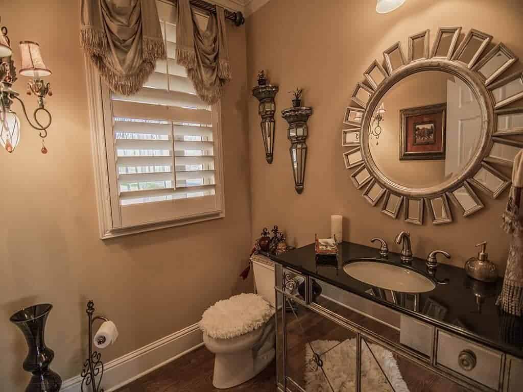 优雅的化妆室设有一面阳光反射镜安装在镜面洗手台梳妆台上方，白色蓬松地毯被反射。它放在木板地板上，与马桶盖互补。