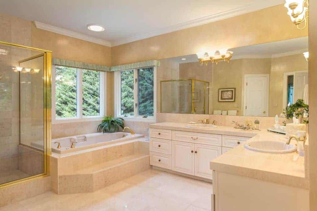 豪华的主浴室展示了一个落地式浴缸和步入式淋浴，金色衬里与安装在无框镜子上的固定装置和烛台互补。