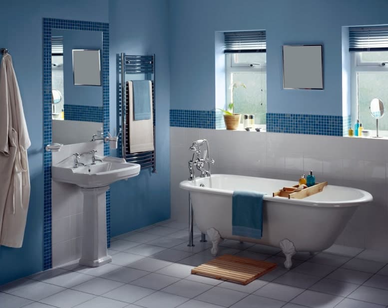 蓝色浴室，底座式洗手池和位于白色瓷砖地板上的爪形浴缸。镜子旁边有不锈钢的固定装置和毛巾架。