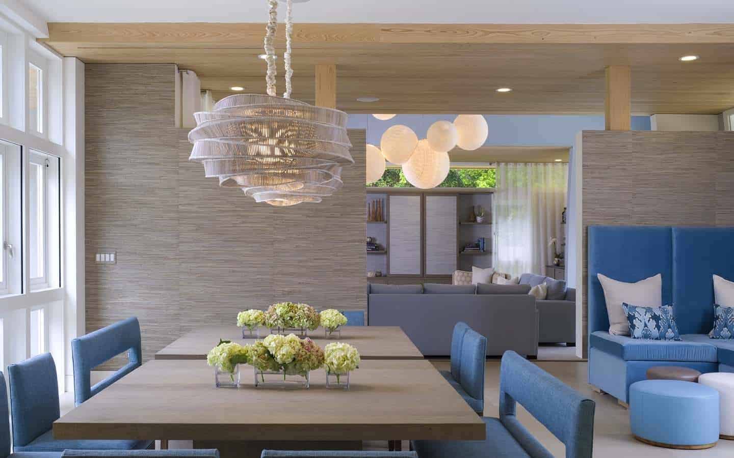 这间通风明亮的厨房有一个裸露的木质天花板，搭配着棕色的木墙，与方形餐桌相匹配，餐桌上有一个带有乡村风帽的奇特吊灯。这些与蓝色天鹅绒椅垫形成对比。