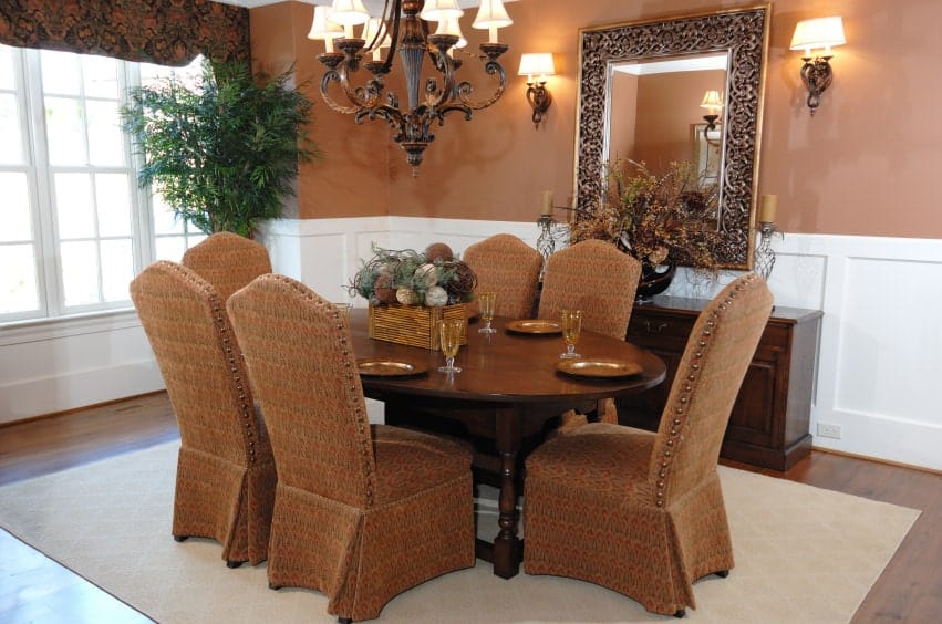这是棕色和白色元素的优雅融合，棕色图案的椅套与与护墙板形成对比的棕色上墙相匹配。还有一盏棕色的锻铁枝形吊灯，与椭圆形的木桌相呼应。