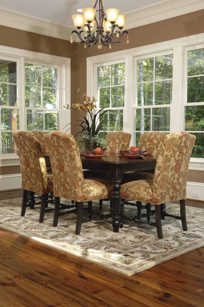 这个别致的餐厅在餐椅上有棕色花卉图案的靠垫，与花卉图案的地毯相匹配，与硬木地板形成对比。它还与窗户照亮的餐桌的深棕色形成对比。
