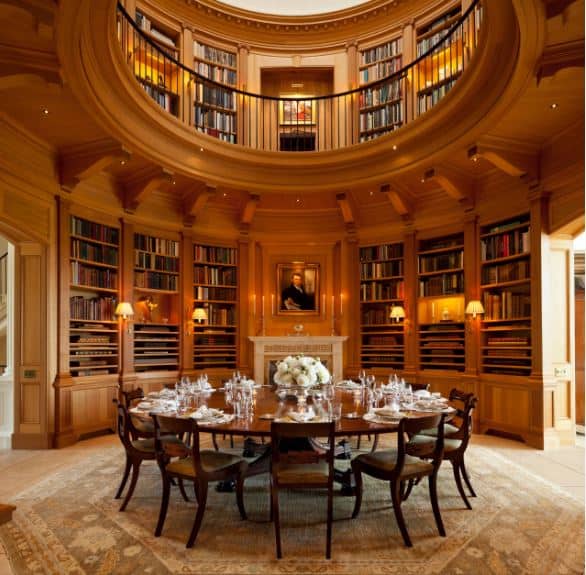 这个独特的餐厅位于一个圆形的两层图书馆的木墙内，墙壁上摆满了书架，墙上装饰着壁灯，壁炉位于大木制圆形桌子旁，周围是浅色图案地毯上的木椅。