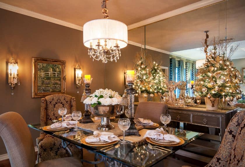 这个优雅的餐厅完全是圣诞模式，一对桌面小圣诞树放在控制台桌子上，与棕色的墙壁相配，棕色软垫餐椅的玻璃面餐桌上有一盏小吊灯。