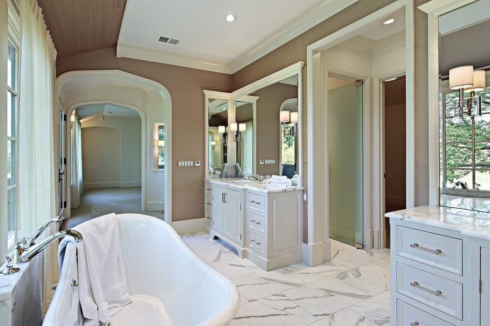 棕色和白色的主浴室设有棕色墙壁和白色大理石瓷砖地板。房间里有两个水槽柜台，还有一个步入式淋浴间和一个独立式浴缸。