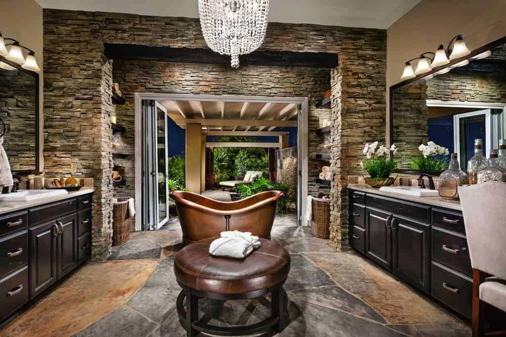 大而优雅的主浴室，设有一个青铜色的独立式浴缸，两个水槽柜台，中间有一把大奥斯曼椅，由一盏华丽的枝形吊灯照亮。