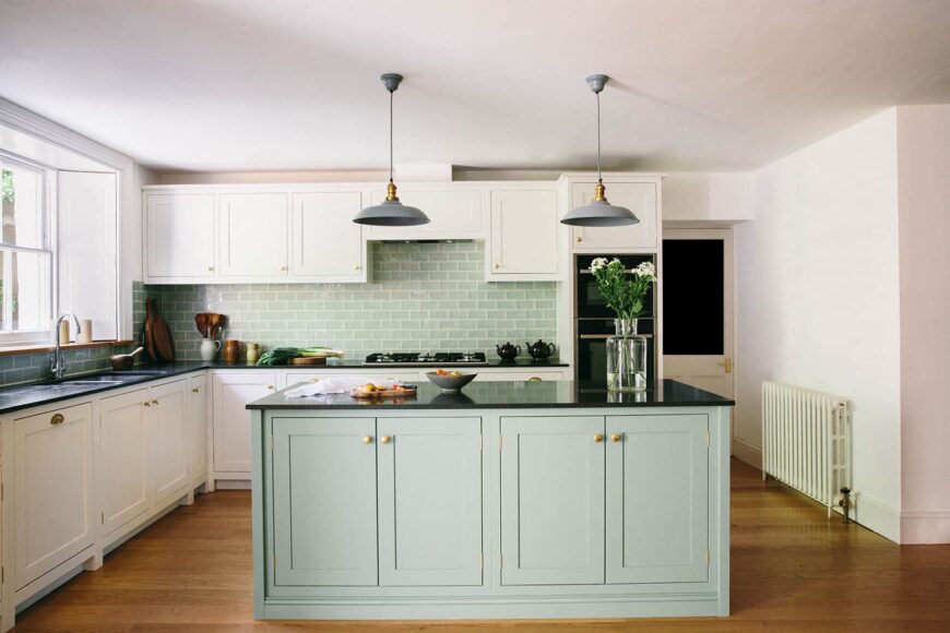 现代厨房配有定制黄铜把手的白色橱柜和配套的蓝色瓷砖后挡板和厨房岛。