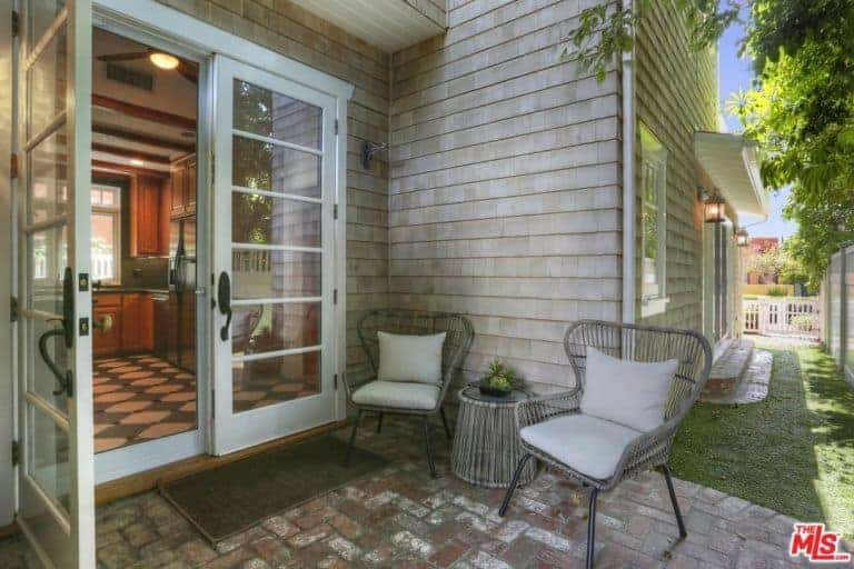 一对浅灰色编织柳条扶手椅有浅灰色的靠垫，在房子的一侧，白色玻璃门外，与红砖地板形成了鲜明的对比，这是一个舒适的放松区。