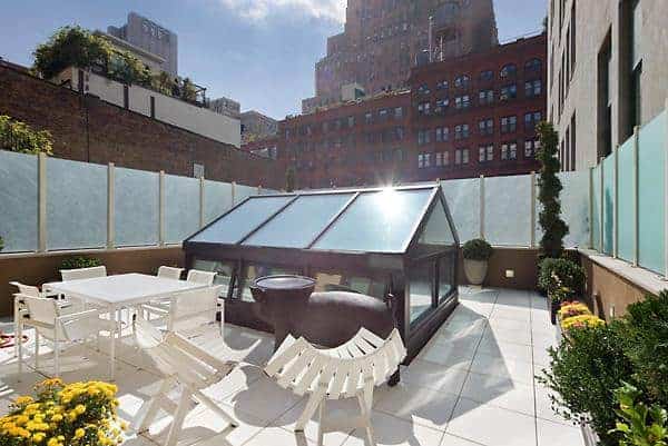 这是一个屋顶露台，周围环绕着磨砂玻璃板，以保护隐私。这是软化了各种盆栽植物和<a class=