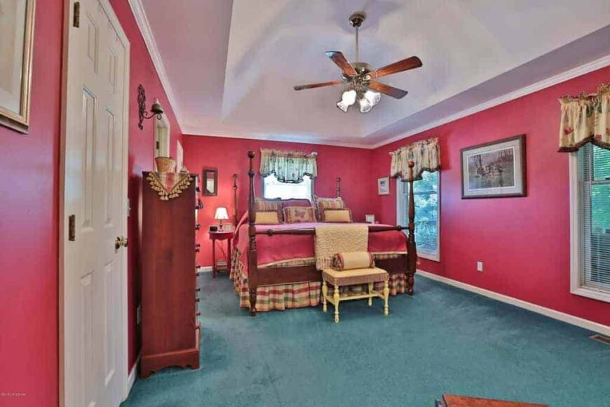 乡村风格的主卧室，红色的墙壁和绿色的地毯地板。它提供了一个大的优雅的床和侧面的橱柜。