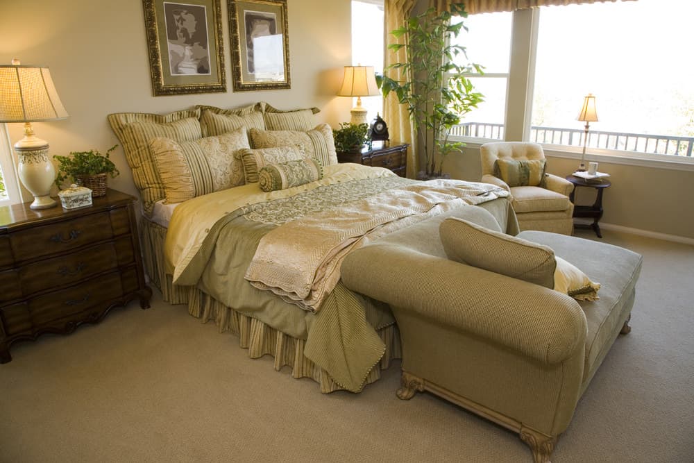 这张照片聚焦在主卧室的大床上，床边有一张沙发。床的布置由几盏看起来很优雅的台灯照亮。