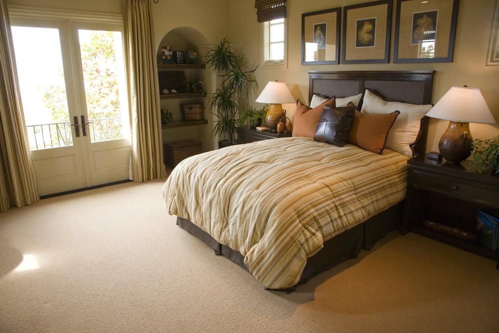 宽敞的主卧室设有一个优雅的床设置以及侧面的内置架子。房间有高高的天花板和铺着地毯的地板。
