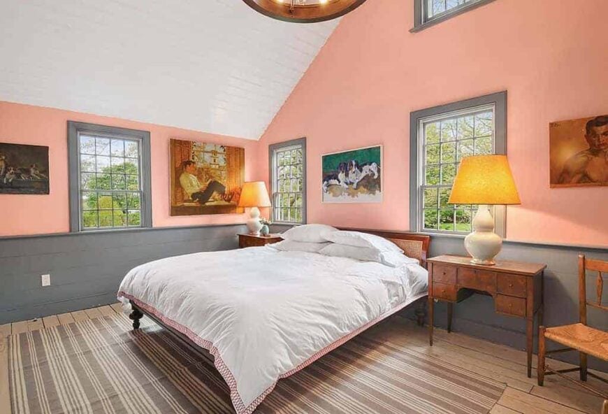 乡村风格的主卧室设有橙色的墙壁和硬木地板，上面有一块区域地毯，以及高高的白色天花板。床的两侧都有台灯照明。
