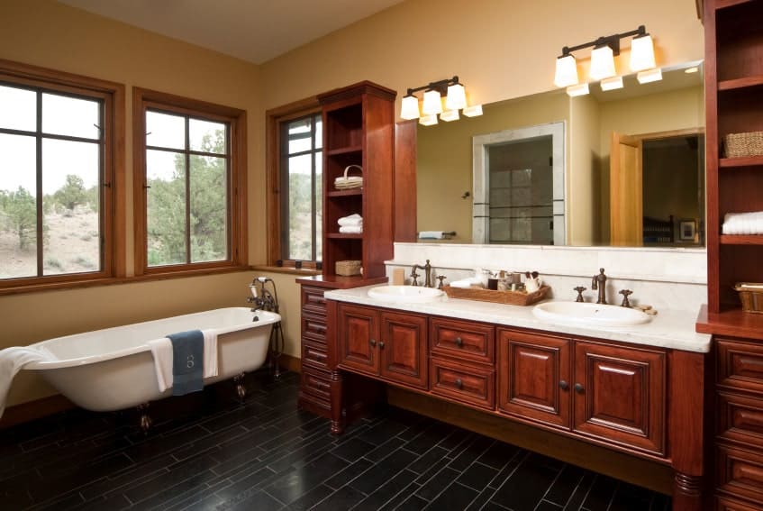 这个工匠风格的浴室的黑色地砖与大型深色木结构相辅相成，设有两个洗手台，洗手台有优雅的橱柜和抽屉，白色台面与白色独立式浴缸形成对比。