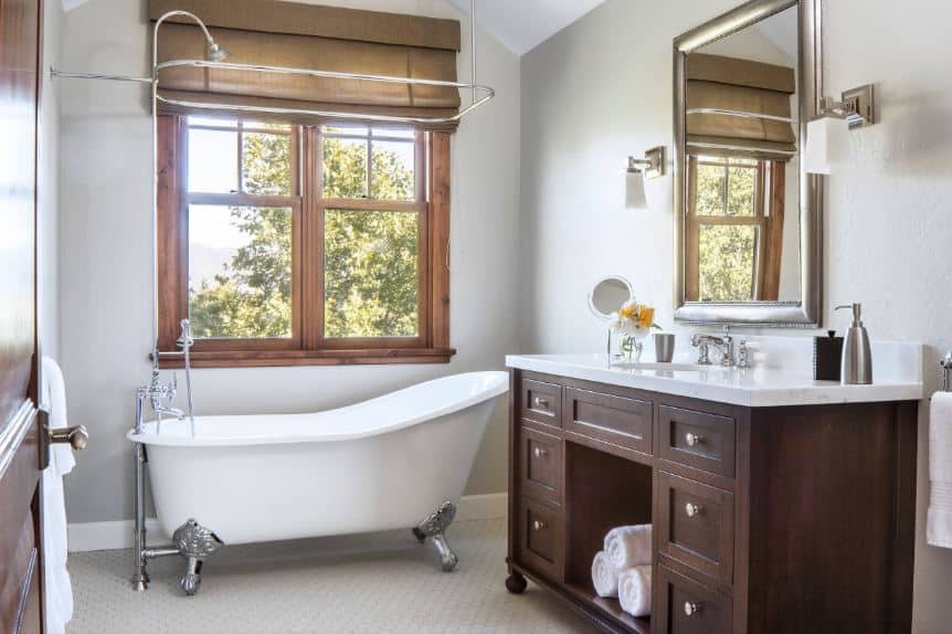 白色独立式浴缸配有不锈钢桌腿，与浴室的管道、镜框和固定装置以及黑色梳妆台上优雅木制抽屉的把手相匹配，与白色台面形成对比。
