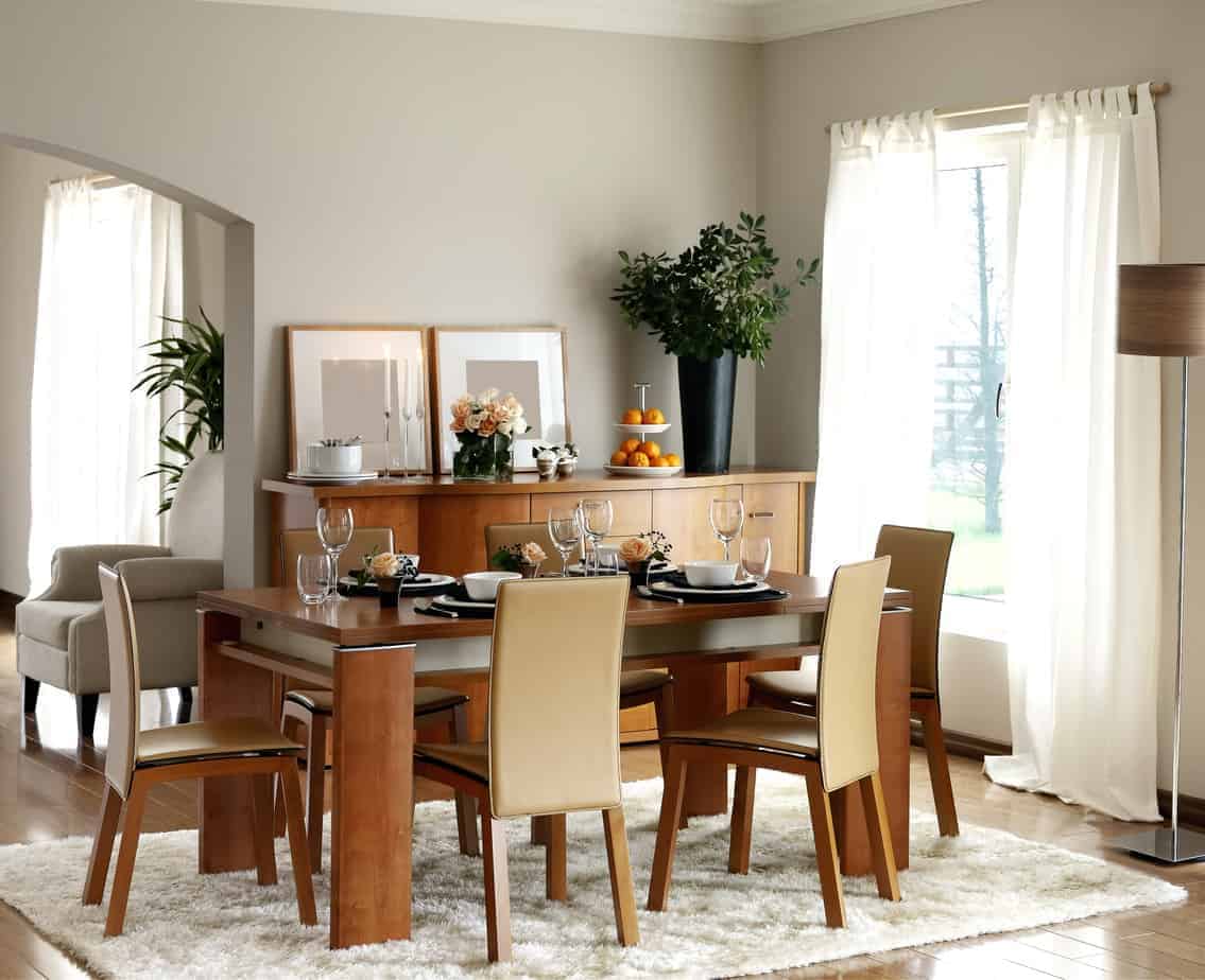 木制餐具与自助餐桌相得益彰，餐桌顶部有框墙艺术和一个黑色花瓶。它有白色的蓬松地毯，透明的窗帘覆盖着玻璃窗户。