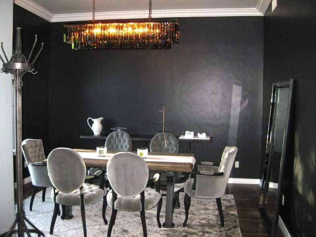 黑色的餐厅展示了灰色的簇绒椅子和天然木材餐桌，餐桌上有白色的桌布。它包括一盏别致的线性吊灯、一面大镜子和一张与墙壁融为一体的自助餐桌。