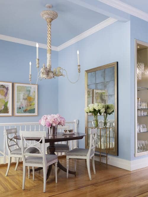 迷人的餐厅展示了可爱的艺术品和镶嵌在天蓝色墙壁上的镜子。餐厅里有一盏蜡烛枝形吊灯，深色木质餐桌周围有条纹软垫椅子。