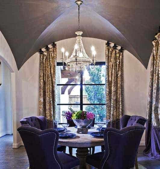 紫色的簇绒椅子为这个优雅的餐厅增添了一个漂亮的口音，拥有一个圆形的餐桌和一个从拱形天花板上悬挂的水晶吊灯。