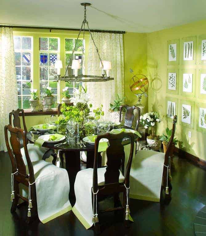 新鲜的餐厅设计，植物画廊安装在绿色的墙壁上。它有一盏圆形吊灯和一套深色的木制餐具，上面点缀着盆栽。