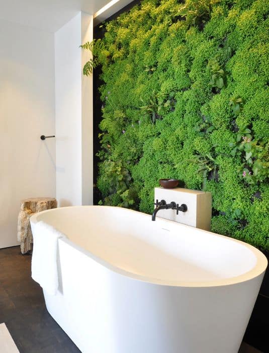 宁静的浴室设有一个光滑的独立式浴缸，配有锻铁装置，绿色生活墙强调，为房间创造了清爽的氛围。