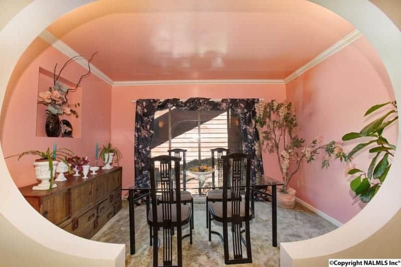 不拘一格的餐厅，粉色的墙壁和天花板。有一张方形的玻璃餐桌，上面有四个现代化的座位。在房间的两个角落也有室内盆栽。