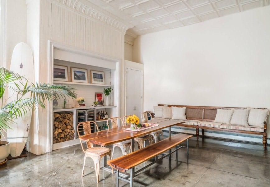 宽敞的餐厅设有木质餐桌和木质长凳。有一个长凳，旁边有一对泡沫。房间四周是白色的墙壁和白色的高高的天花板。